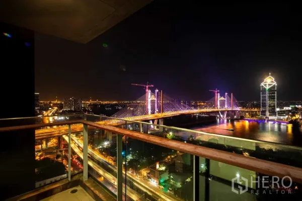 Condominium for sale - High-floor balcony overlooking the illuminated bridge and riverside skyline at night.