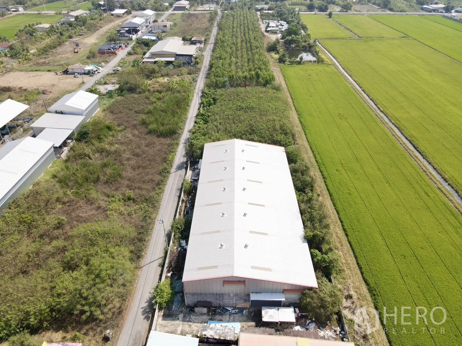 โกดัง for sale in Lam Luk Ka, Pathum Thani - ภาพมุมสูงของโกดังหลังคาเมทัลชีทบนที่ดินกว้าง รายล้อมด้วยทุ่งนาและถนนซอยในลำลูกกา
