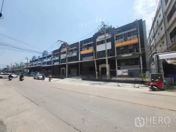 Factory for rent or sale in Samut Prakan - Three-storey industrial row building with gated fronts and scaffolding along a wide street in Bang Phli.