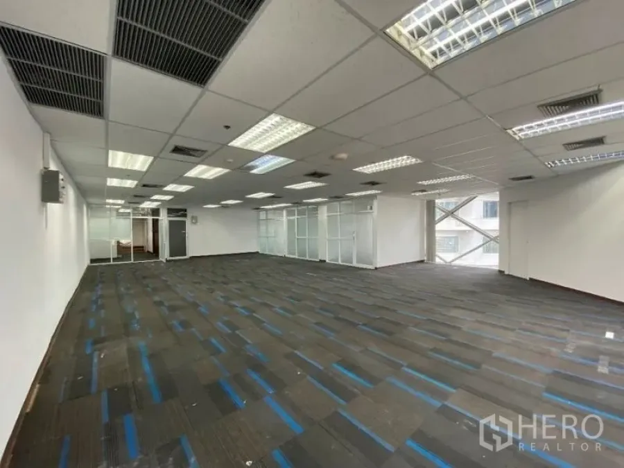 Office Space for rent in Khlong Toei, Bangkok - Spacious open-plan office with blue-striped carpet tiles, drop ceiling, fluorescent lighting and glass-partitioned rooms.