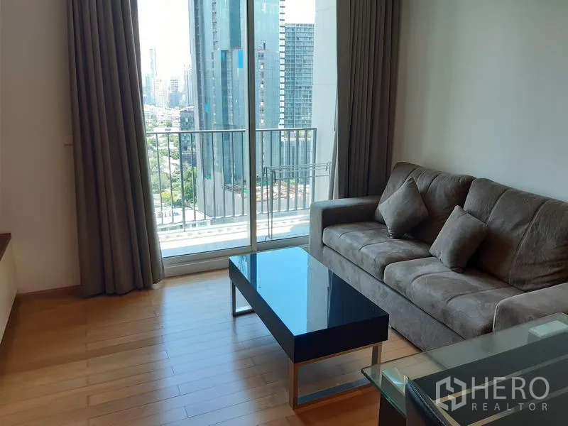 คอนโด ให้เช่าในKhlong Toei, Bangkok - ห้องนั่งเล่นสว่าง โซฟาสีเทา โต๊ะกลางกระจก และระเบียงมองเห็นสกายไลน์กรุงเทพฯ