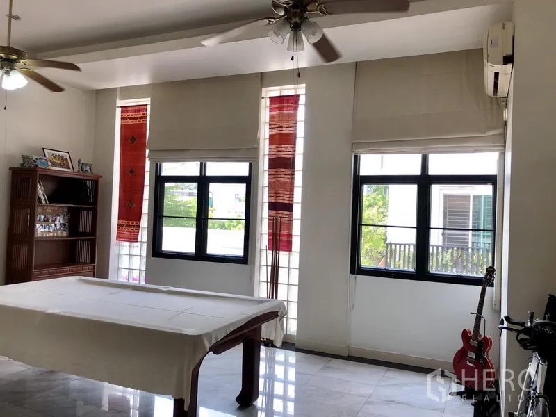 ทาวน์เฮาส์ ให้เช่าหรือขายในBangkok - ห้องเอนกประสงค์สว่าง หน้าต่างหลายบาน พัดลมเพดาน โต๊ะ และชั้นวางของพร้อมกีตาร์