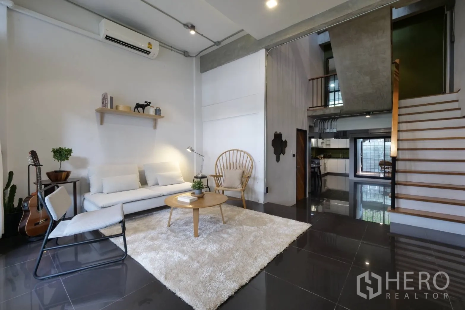 Townhouse for rent in Khlong Toei, Bangkok - High-ceiling living room with white sofa, rug and open staircase.