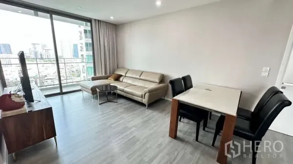 Condominium for rent - Bright living and dining area with a four-seat table beside large glass balcony doors overlooking Bangkok.