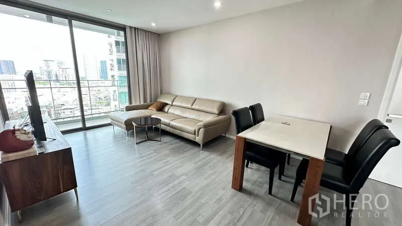 Condominium for rent - Bright living and dining area with a four-seat table beside large glass balcony doors overlooking Bangkok.