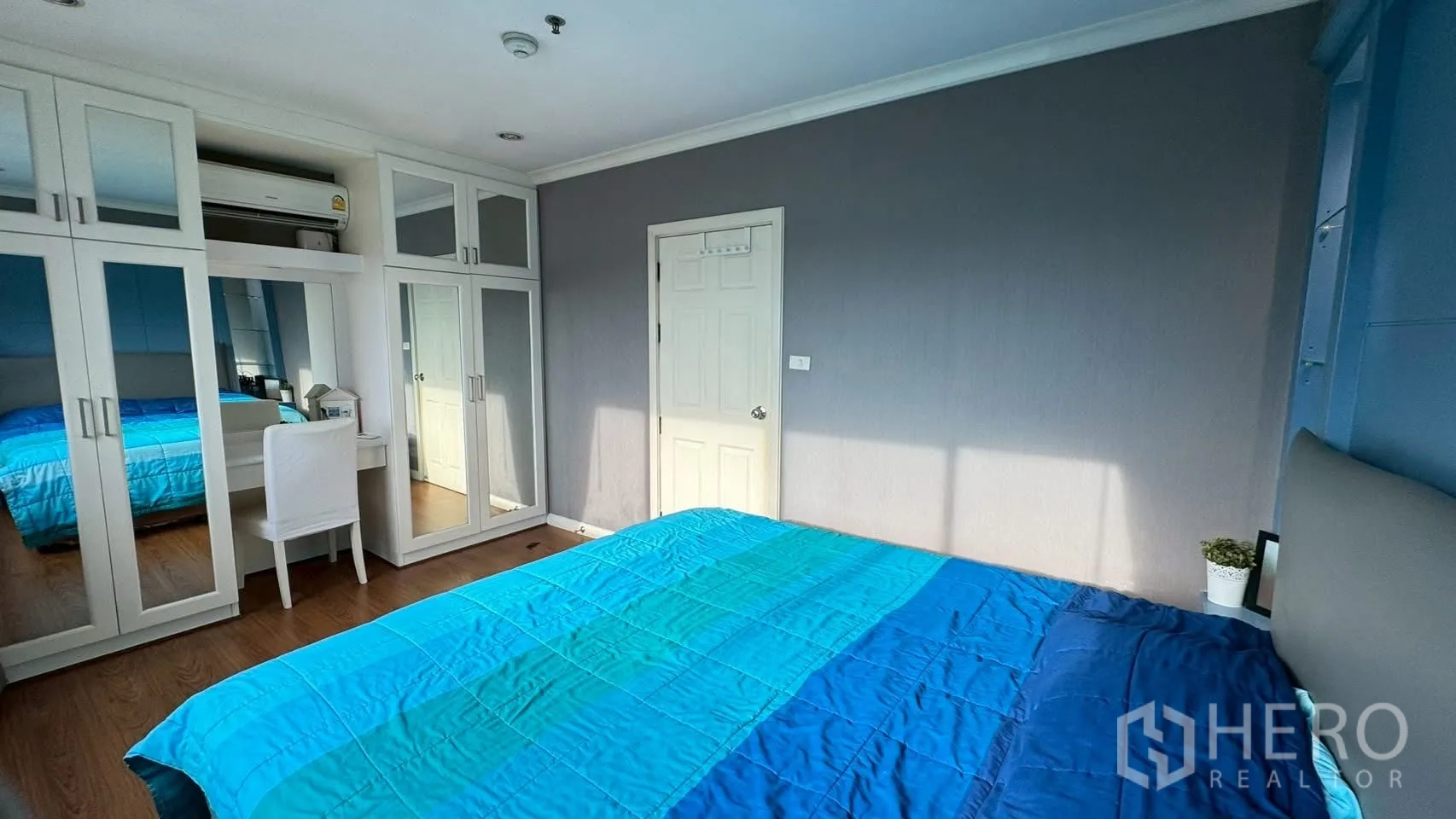Condominium for rent or sale in Watthana, Bangkok - Master bedroom wall with white wardrobes, dressing table and sunlit gray wall.