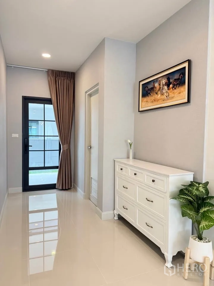 Detached House for rent in Bang Phli, Samut Prakan - Neat hallway with white chest of drawers, artwork, and door to the yard.
