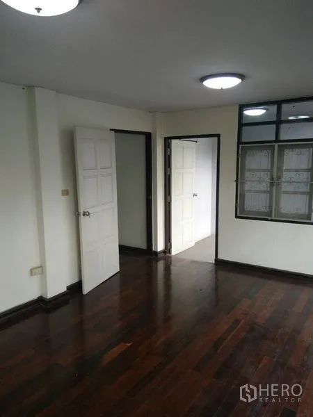 Townhouse for rent in Phra Khanong, Bangkok - Upper floor room featuring dark wooden flooring, windows with grilles and white doors.