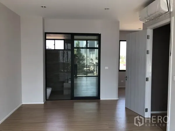 Townhouse for sale in Saphan Sung, Bangkok - Spacious bedroom with wood flooring, air conditioner, and an ensuite behind a glass sliding door.