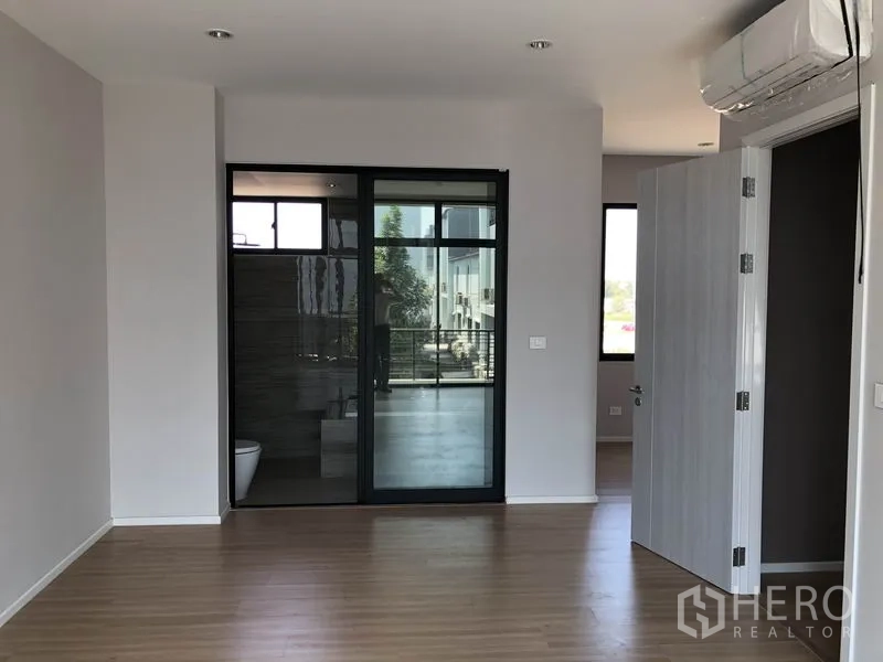 Townhouse for sale in Saphan Sung, Bangkok - Spacious bedroom with wood flooring, air conditioner, and an ensuite behind a glass sliding door.