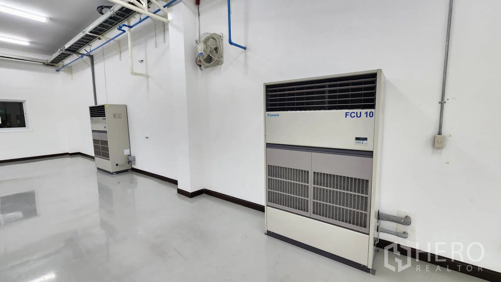 Factory for sale in Bang Bo, Samut Prakan - Interior wall with emergency exit door, windows and surface-mounted conduits.