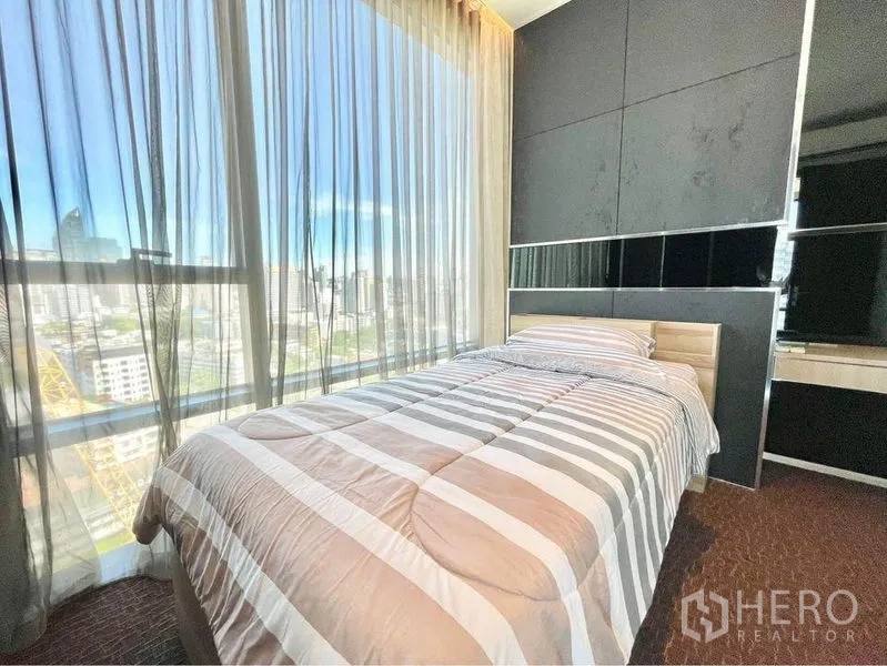 Condominium for rent in Watthana, Bangkok - Second bedroom with single bed and floor-to-ceiling windows with sheer curtains and Bangkok city view.