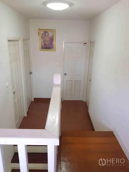 Detached House for sale in Nonthaburi - Upper hallway with white doors, railing and wood flooring.