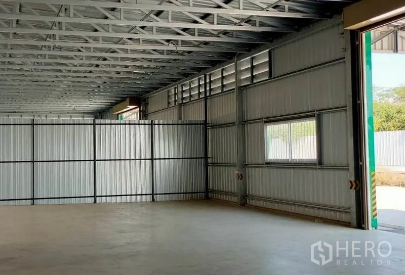 Warehouse for rent in Pak Kret, Nonthaburi - Interior of the warehouse showing steel truss roof, side windows, smooth concrete floor, and a large opening.