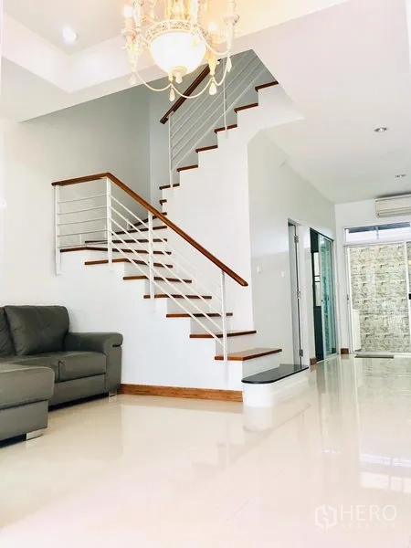 联排别墅 出租在Prawet, Bangkok - 木扶手楼梯与水晶灯，旁边是宽敞客厅。