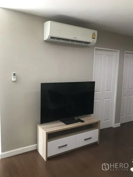Condominium for rent or sale in Huai Khwang, Bangkok - Living area wall featuring split-type air conditioner above a TV on a modern media console.