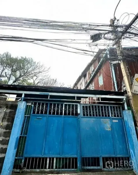 Shophouse for rent in Bang Rak, Bangkok - Blue metal gate and fence of a Bang Rak shophouse entrance on a quiet lane with overhead utility cables.
