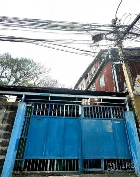 Shophouse for rent in Bang Rak, Bangkok - Blue metal gate and fence of a Bang Rak shophouse entrance on a quiet lane with overhead utility cables.