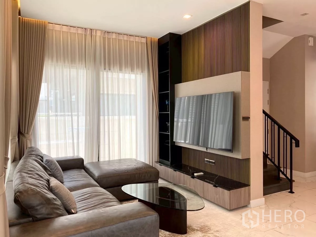 Detached House for rent in Bang Phli, Samut Prakan - Cozy living room with L-shaped leather sofa, wall-mounted TV unit and staircase.