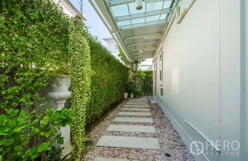 Detached House for rent in Prawet, Bangkok - Side walkway with stepping stones beneath a glass canopy bordered by green hedges.