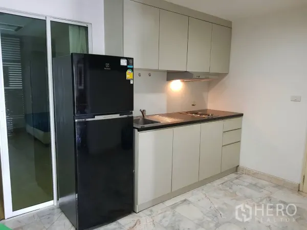 公寓 出租在Khlong Toei, Bangkok - 紧凑厨房，吊柜、灶台、抽油烟机与黑色冰箱，旁有推拉玻璃门