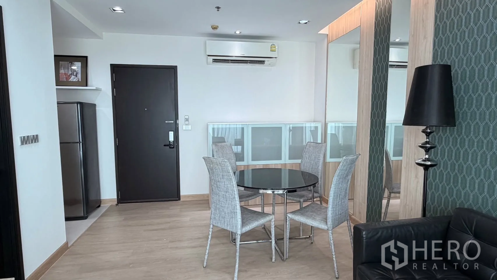Condominium for rent or sale in Watthana, Bangkok - Dining area with round glass table and four chairs next to a mirrored wall and entry door with fridge nook.