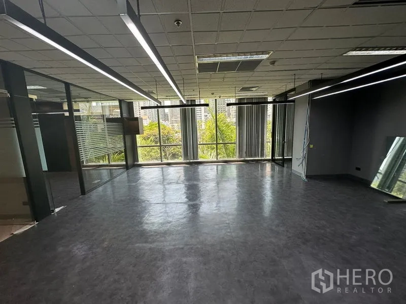 Office Space for rent - Corner office area with linear pendant lighting and full-height windows facing trees.