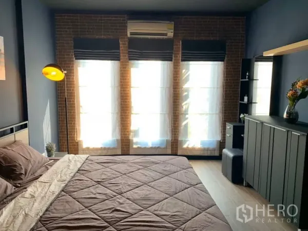 联排别墅 出租在Bang Kapi, Bangkok - 主卧带砖纹特色墙与落地高窗，配空调。