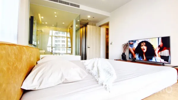 Condominium for rent or sale in Watthana, Bangkok - Bedroom view toward a glass-walled bathroom and a media console with a flat-screen TV.