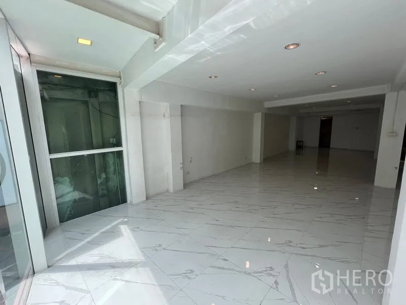 พื้นที่ขายปลีก ให้เช่าในKhlong Toei, Bangkok - ฮอลล์โชว์รูมยาว เพดานฝังไฟ ผนังสีขาว และลิฟต์กระจกใกล้ทางเข้า.