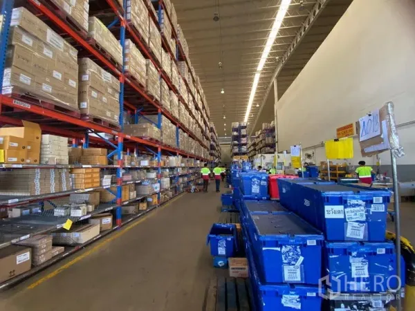 Warehouse for rent in Bang Phli, Samut Prakan - Long high-ceiling aisle lined with racking and plastic bins under strip lights.
