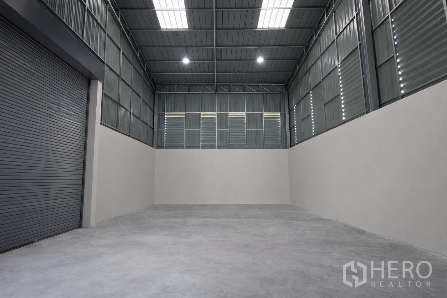 Warehouse for rent in Bang Kapi, Bangkok - High-ceiling storage bay with concrete floor, metal cladding, skylights and a large roller door.