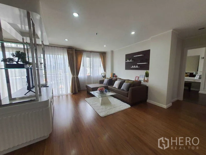 房间 出租在Watthana, Bangkok - 宽敞起居区，转角沙发、墙面置物架与城市景观窗