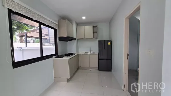 Townhouse for rent or sale in Saphan Sung, Bangkok - U-shaped kitchen with window, cabinetry, refrigerator and doorway to a guest bathroom.