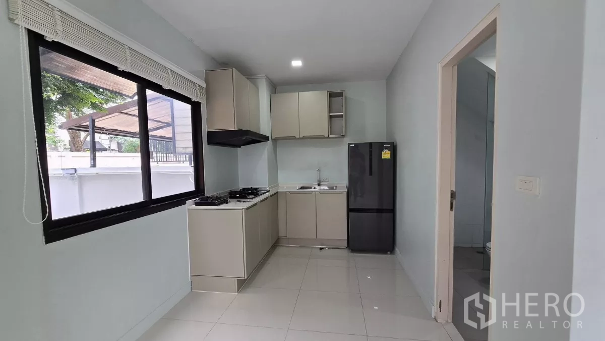 Townhouse for rent or sale in Saphan Sung, Bangkok - U-shaped kitchen with window, cabinetry, refrigerator and doorway to a guest bathroom.