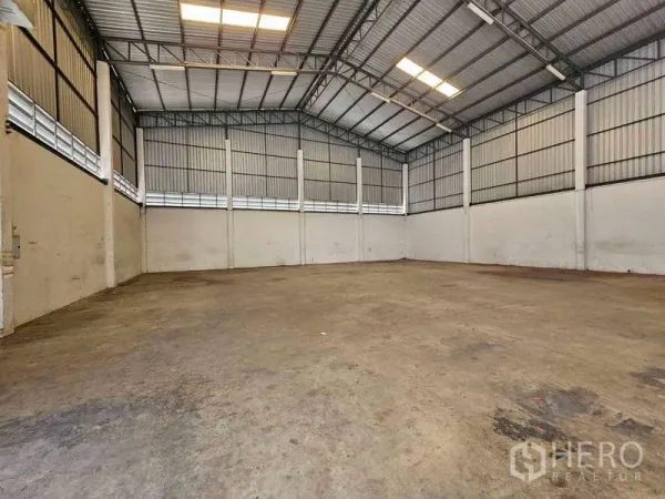 Warehouse for rent in Bang Bua Thong, Nonthaburi - Open warehouse interior showing a high clear-span steel roof, skylights, and concrete flooring.