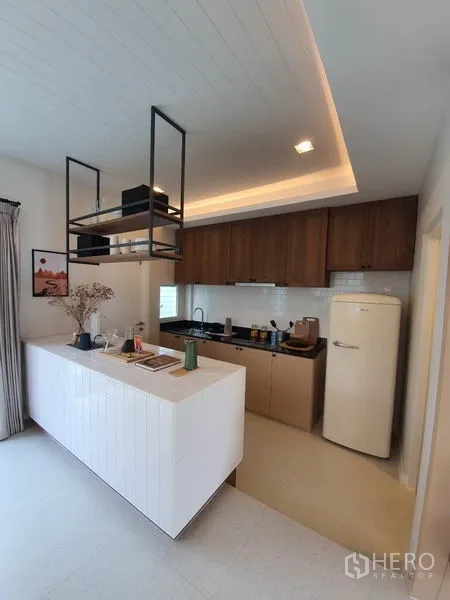 Detached House for rent in Prawet, Bangkok - Modern kitchen with white island, wood cabinets, hanging shelves and retro-style fridge.