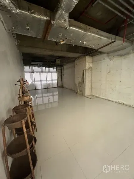 零售空间 出租 - 空置店铺内部，高挑裸顶、白色地面，侧墙摆放木质陈列架。