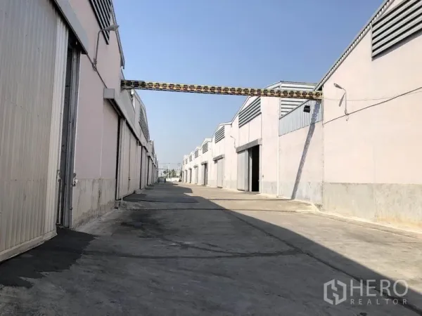 Warehouse for rent in Bang Bua Thong, Nonthaburi - Wide service road between parallel warehouse blocks with overhead conduit and loading bays.