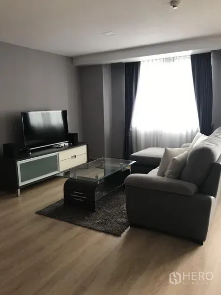 公寓 出租在Bang Rak, Bangkok - 舒适客厅，电视柜与平板电视、玻璃茶几和木地板。