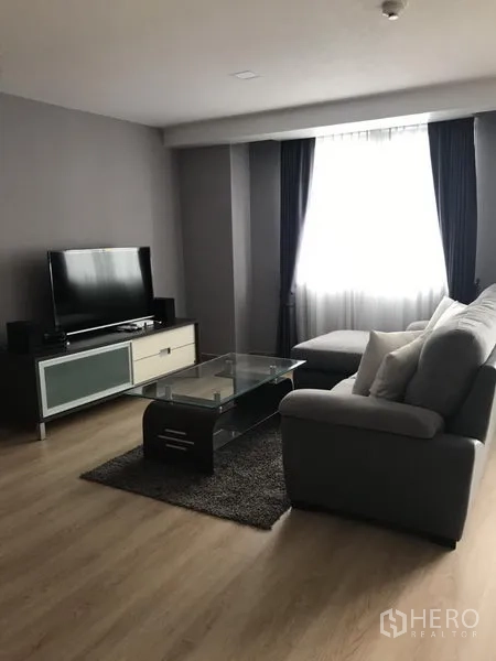 公寓 出租在Bang Rak, Bangkok - 舒适客厅，电视柜与平板电视、玻璃茶几和木地板。