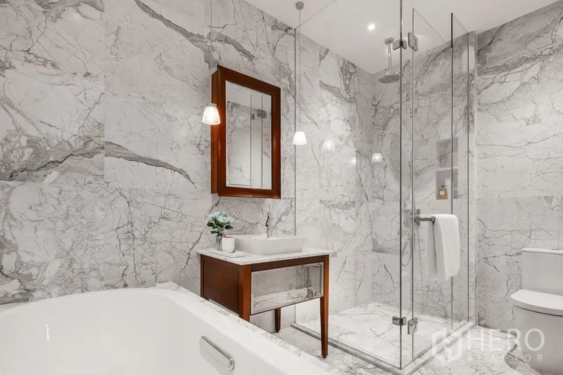 Condominium for sale in Watthana, Bangkok - Luxury bathroom with full marble walls, glass shower enclosure, and soaking tub.