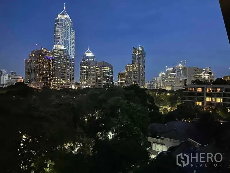 公寓 出租在Pathum Wan, Bangkok - 从阳台望出去的夜晚城市天际线与树梢景观。