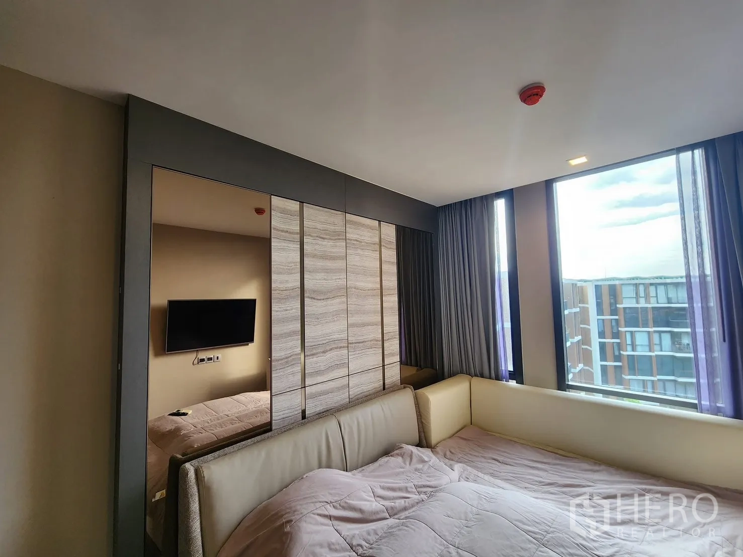 Condominium for rent in Watthana, Bangkok - Cozy bedroom with large window, built-in wardrobe, and wall-mounted TV overlooking the courtyard.