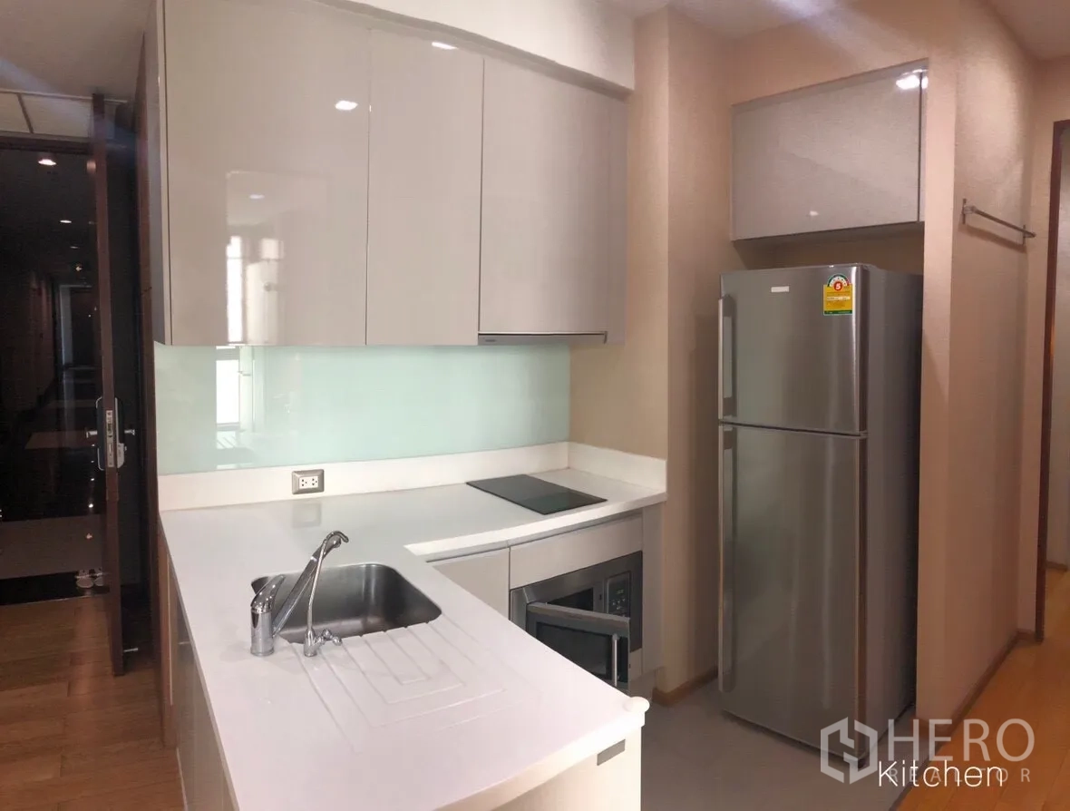 公寓 出租或出售在Ratchathewi, Bangkok - 现代白色厨房，亮面柜体、电磁炉、水槽与不锈钢冰箱。