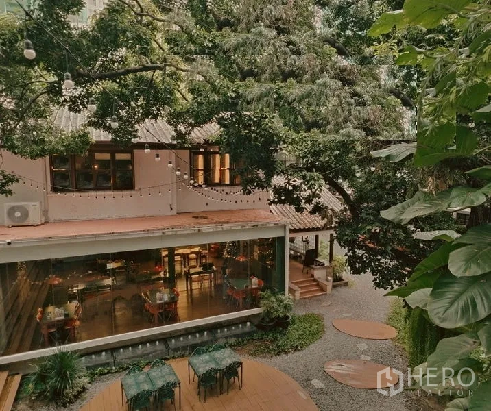 零售空间 出租在Pathum Wan, Bangkok - 玻璃立面的用餐大厅通向绿意庭院，串灯与座位。