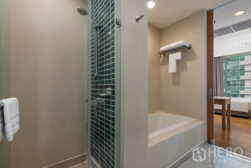 Condominium for rent in Bang Kho Laem, Bangkok - Bathroom featuring a glass shower beside a built-in bathtub with warm lighting.