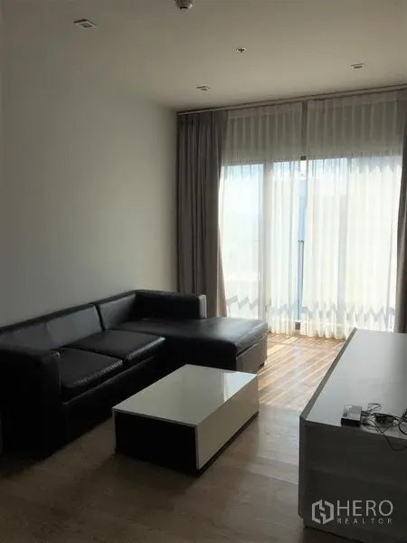 คอนโด ให้เช่าในBangkok - ห้องนั่งเล่นสว่าง โซฟาหนังทรง L โต๊ะกลาง และผ้าม่านโปร่งแบบเต็มผนัง