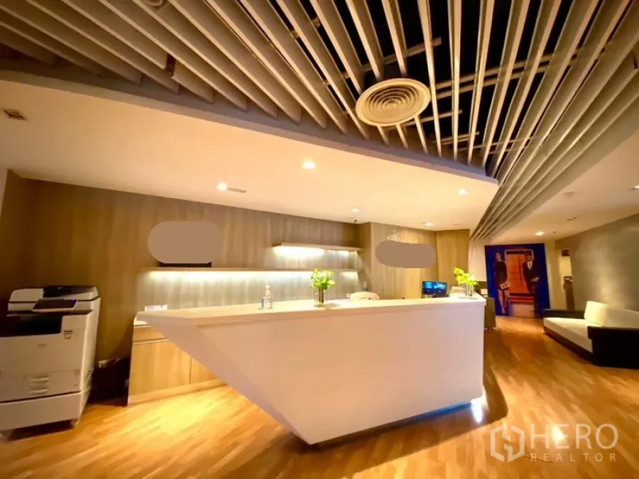 Office Space for rent in Watthana, Bangkok - Contemporary reception area featuring an angular white counter, wood paneling, decorative ceiling baffles, and soft ambient lights.