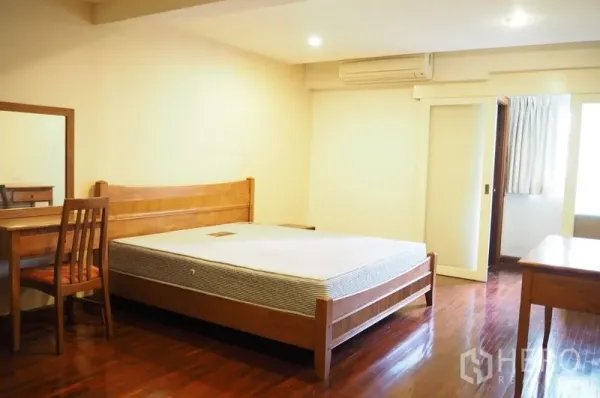 Condominium for rent in Pathum Wan, Bangkok - Spacious bedroom with wooden bed, desk and door to ensuite bathroom